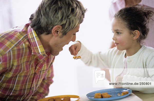 Girl feeding father with fish sticks