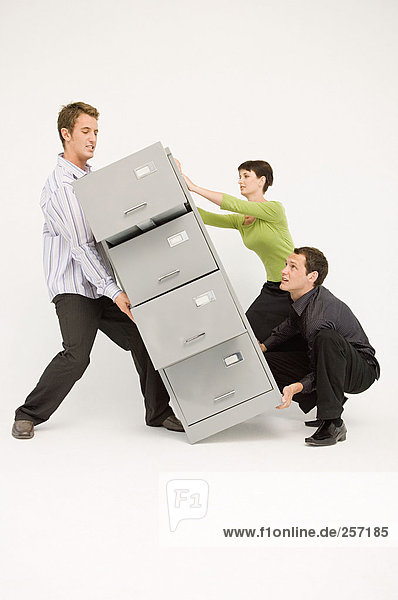 Three office workers lifting heavy filing cabinet