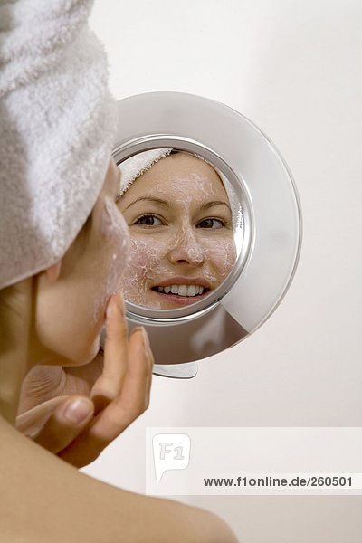 Junge Frau mit Gesichtsmaske im Spiegel lächelnd