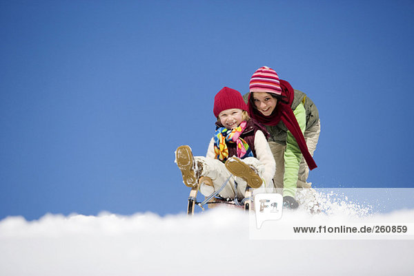 Austria  Teenage girl (16-17) pushing girl (6-7) on sledge  smiling  low angle view