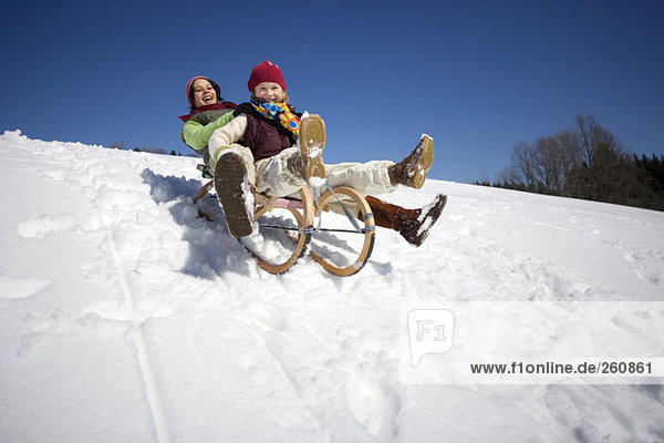 Austria  girls (6-17) sledging on snow covered slope  smiling  low angle view