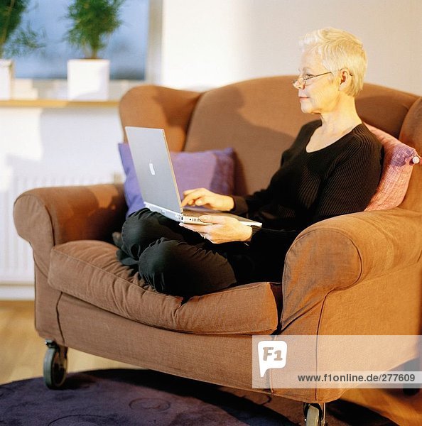 Eine Frau mit einem Laptop in einem Arm-Stuhl.