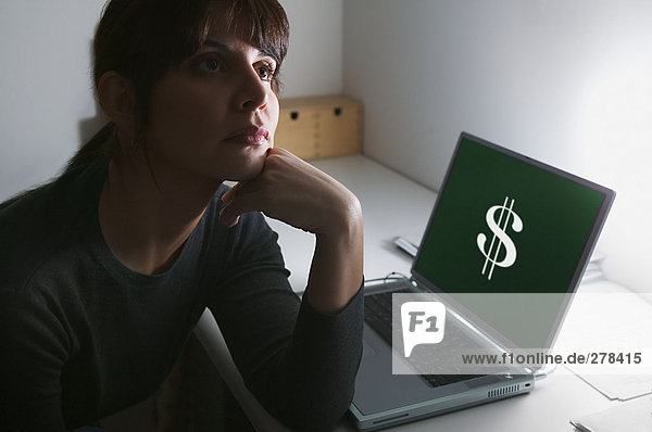 Frau tagträumt mit Dollarzeichen auf ihrem Laptop