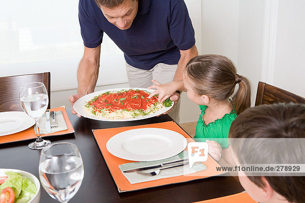 Girl taking spaghetti as father tries to serve meal