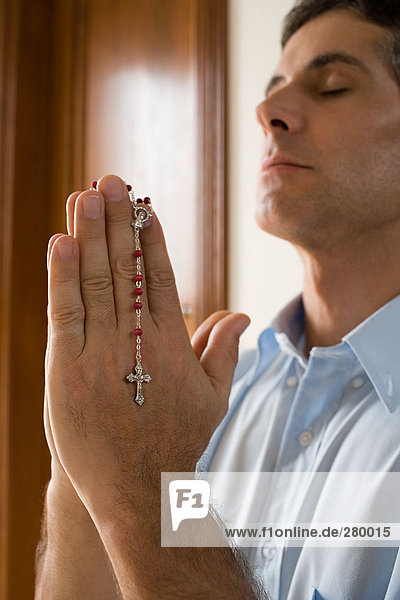 Mann betet mit Rosenkranz