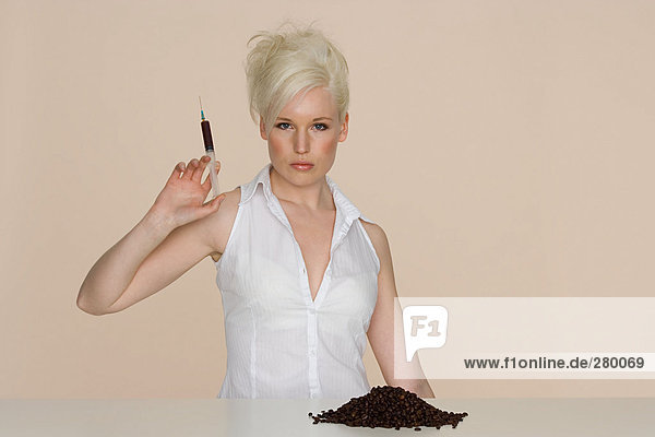 Junge Frau hält eine mit Kaffee gefüllte Spritze.