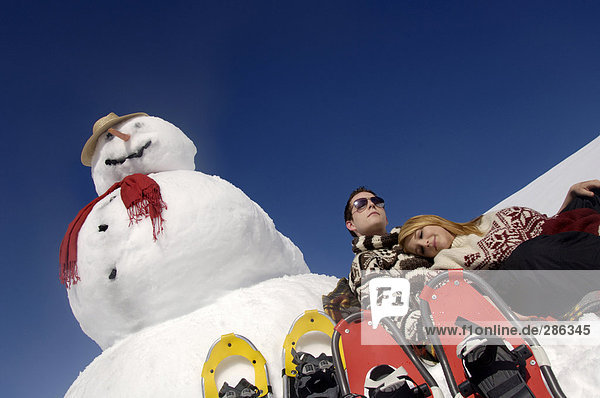 Junges Paar auf Schneemann gelehnt mit Schneeschuhen  Tiefblick