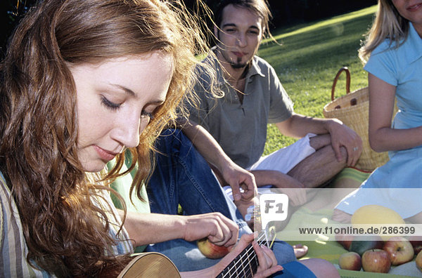 Junge Frau spielt Gitarre für Freunde im Garten  Nahaufnahme