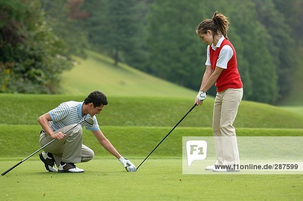 Männlichen Golfspieler legt einen Golfschläger gehalten von einem weiblichen Partner vor Ort tee
