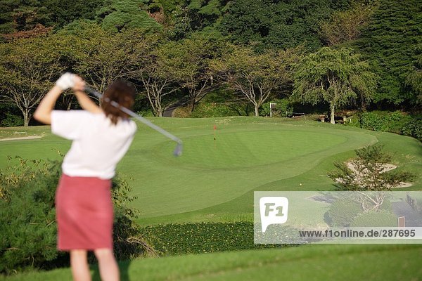 Junge Frau spielt Golf gegen eine Landschaft