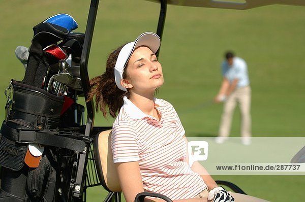 Weibliche Golfer fangen einige Sonnenschein während ihr Partner ein Schuss spielt