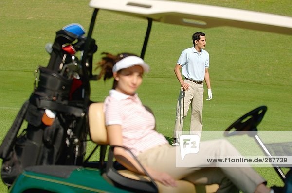 Männlichen Golfspieler Betrachtung des Kurs während seiner Partner in einem Golf-Cart sitzt