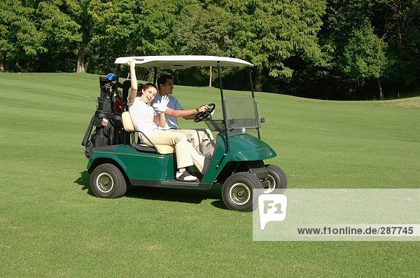 Seitenansicht einer Frau winken während ihr Partner ein Golf-Cart-Laufwerke