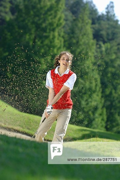 Sand explosion as a female golfer plays a bunker shot