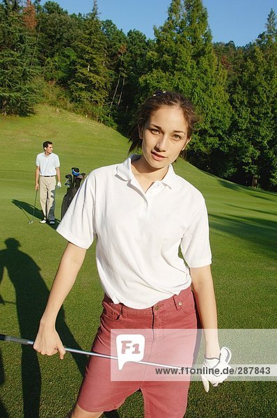 Weibliche Golfer posiert mit ihrem Partner im Hintergrund