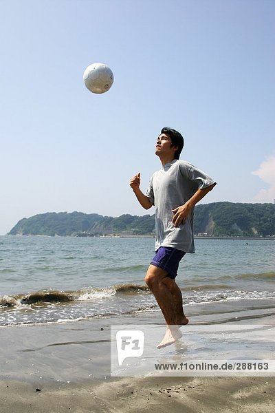 Junger Mann spielen Fußball am Strand