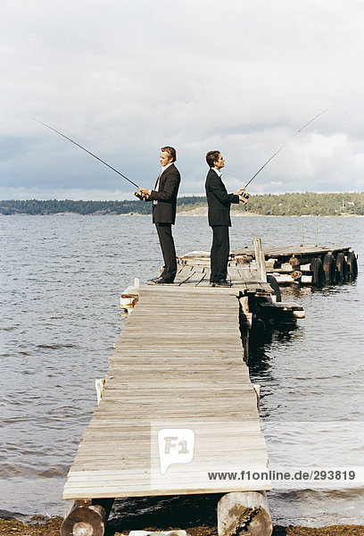 Zwei Männer in Anzügen Angeln von einer Brücke gekleidet.