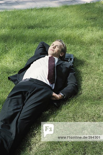 A businessman resting on a lawn.