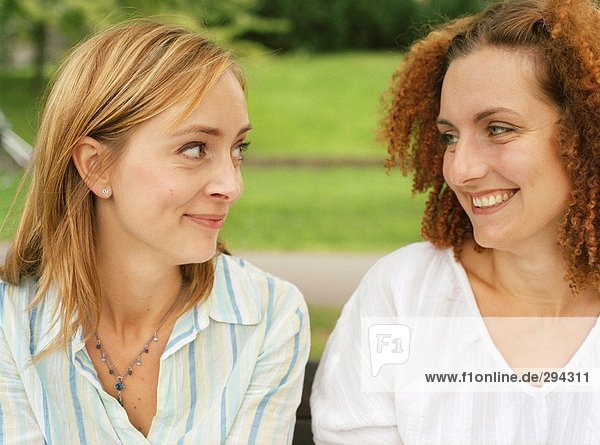 Two smiling women sitting outdoors and looking into each others eyes.