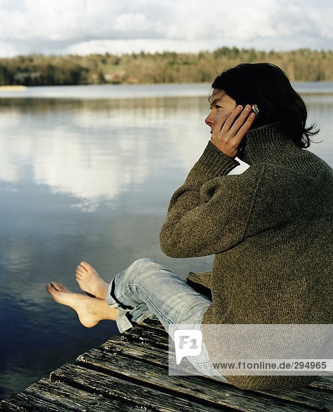 Eine Frau sitzt auf einer Brücke sprechen auf einem Mobiltelefon.