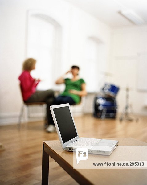 Zwei Personen in einem Raum mit einem Laptop für eine Tabelle im Vordergrund sitzt.