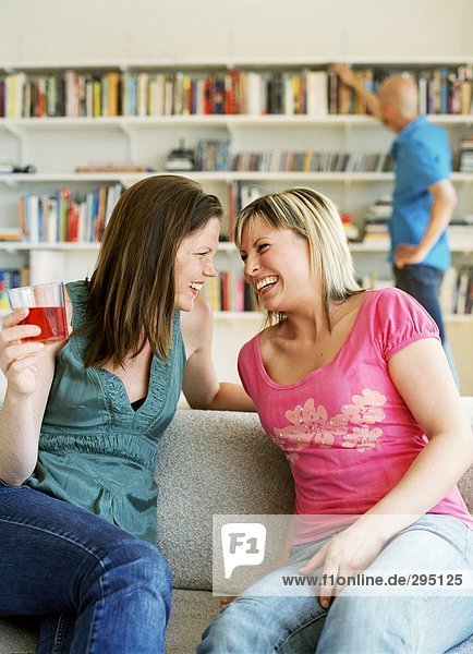 Zwei Frauen in einem Sofa lachen.