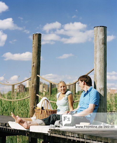 Ein junger Mann und eine junge Frau sitzt auf einer Holzbrücke reden.