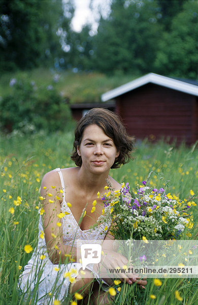Eine Frau sitzend im Gras mit Blumen in der Hand  Schweden.
