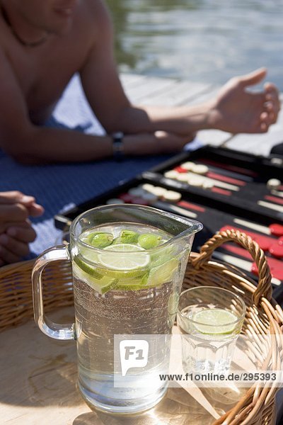 Eine Kanne Wasser und ein Glas mit Stücken von Kalk auf einem Tablett ein Spiel von Backgammon im Hintergrund.