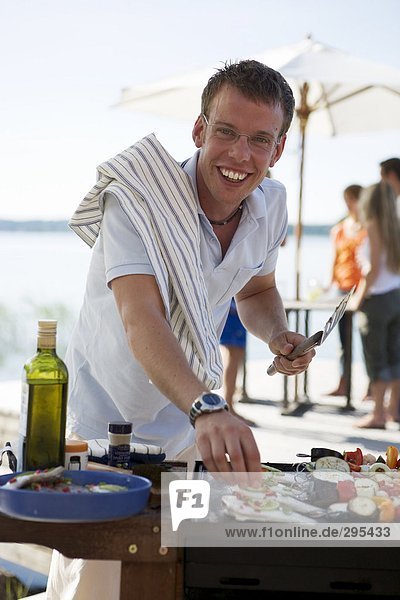A smiling man looking at the camera preparing food on a grill.