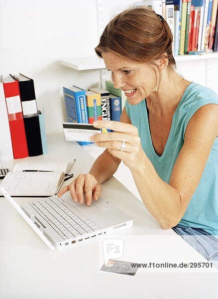 A woman holding a credit card working on a laptop.