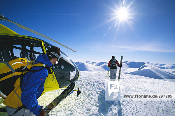 Two skiers by a helicopter in the mountains.
