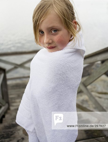 Mädchen eingewickelt in ein Handtuch steht auf einer Mole.