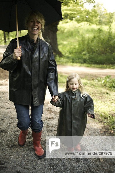 Mutter und Tochter in Regen Kleidung mit einem Regenschirm.