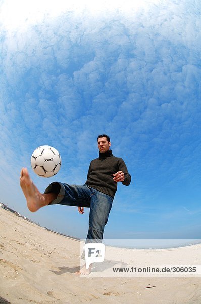 Caucasian male practicing soccer on beach