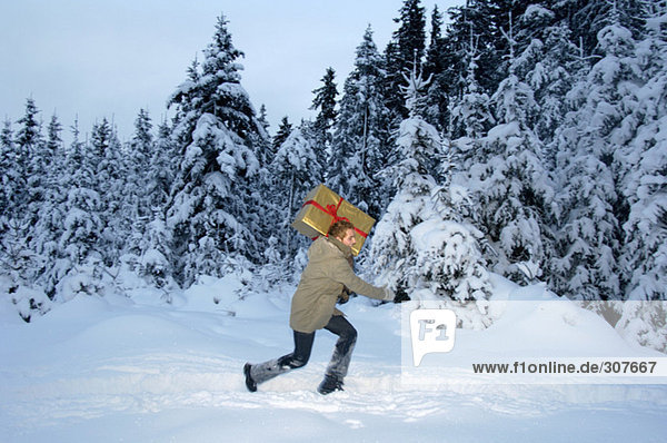 Junger Mann mit Weihnachtsgeschenk im Schnee  Seitenansicht