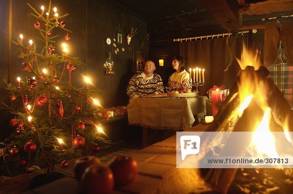 Paar am Tisch in der Almhütte mit Blick auf den Weihnachtsbaum