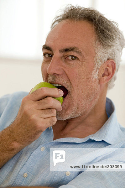 Erwachsener Mann sitzt auf dem Sofa und isst Apfel  Porträt