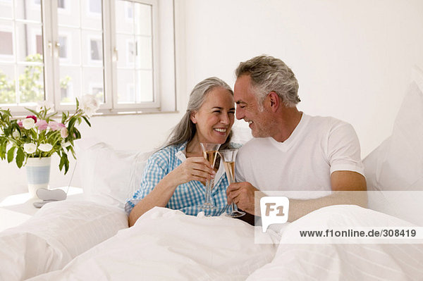 Ein reifes Paar auf dem Bett  das Champagner trinkt  lächelnd