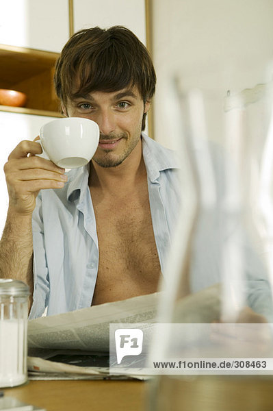 Junger Mann trinkt Kaffee  hält Zeitung lächelnd  Porträt