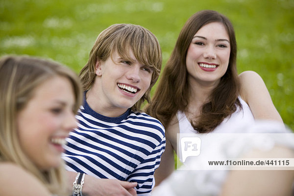 Junge Leute sitzen auf der Wiese und lächeln