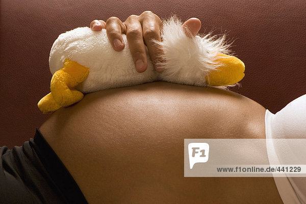 Schwangere mit Plüschtier auf dem Bauch liegend  Seitenansicht  Nahaufnahme