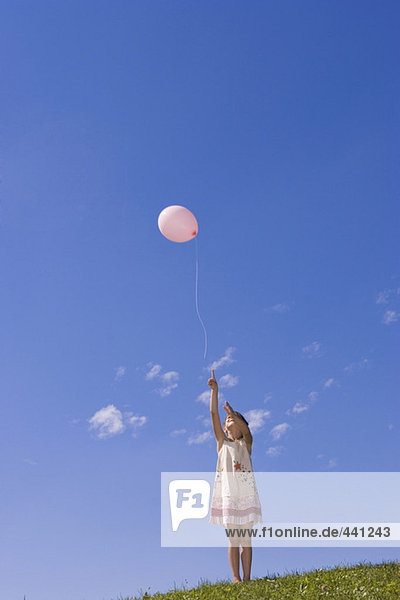 Girl (7-9) standing in meadow  pointing at balloon