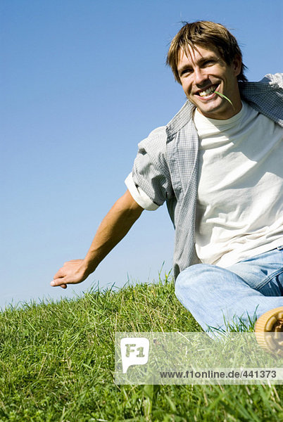 Mittlerer erwachsener Mann sitzt im Park und beißt Gras  lächelnd  niedriger Blickwinkel