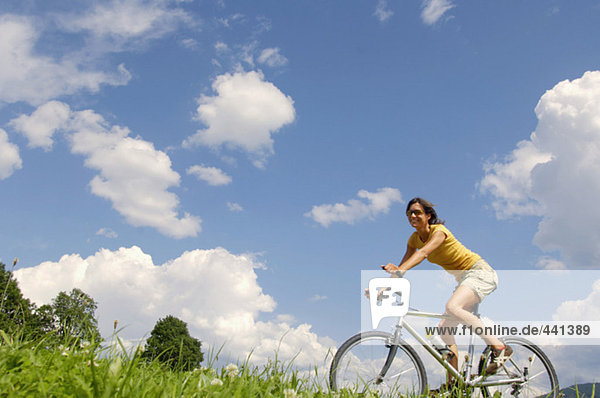 Junge Frau beim Radfahren auf der Wiese,  Seitenansicht