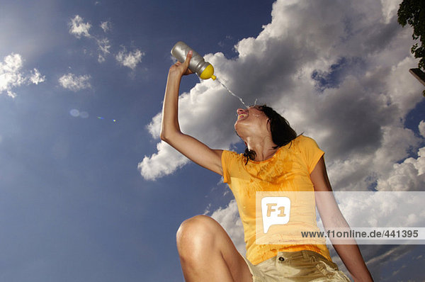 Junge Frau gießt Wasser aus der Flasche ins Gesicht,  Blickwinkel niedrig