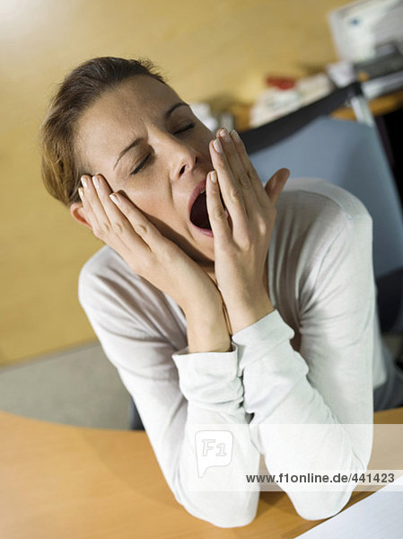 Tired woman sitting at desk  yawning  close-up