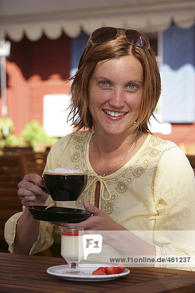 A smiling woman drinking coffee.