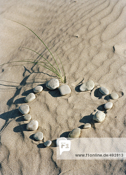 Steine bilden ein Herz im Sand.