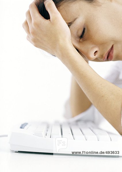 Woman leaning over keyboard holding head